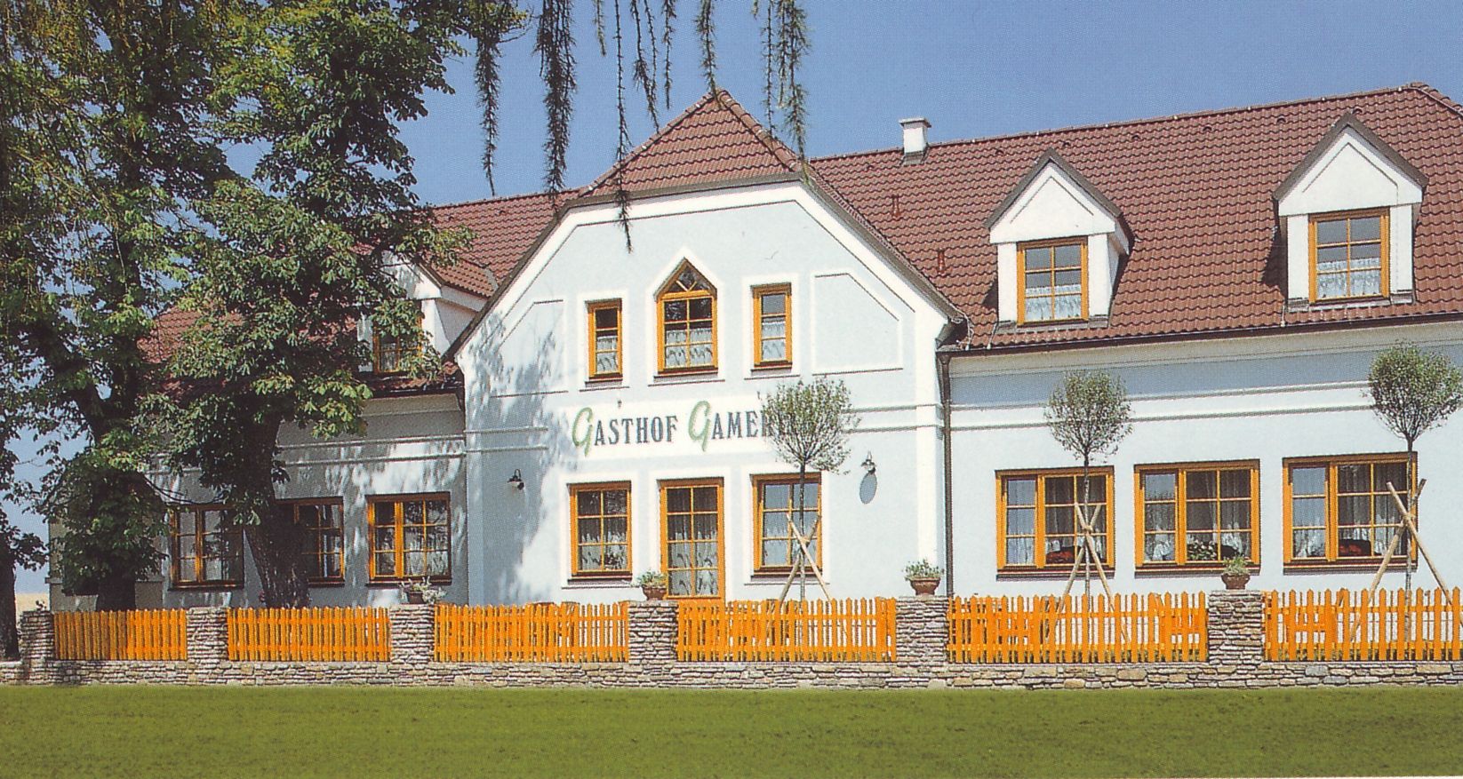 Ein traditionelles Gasthaus mit weißer Fassade und roten Dachziegeln, umgeben von Bäumen und einem Holzzaun.
