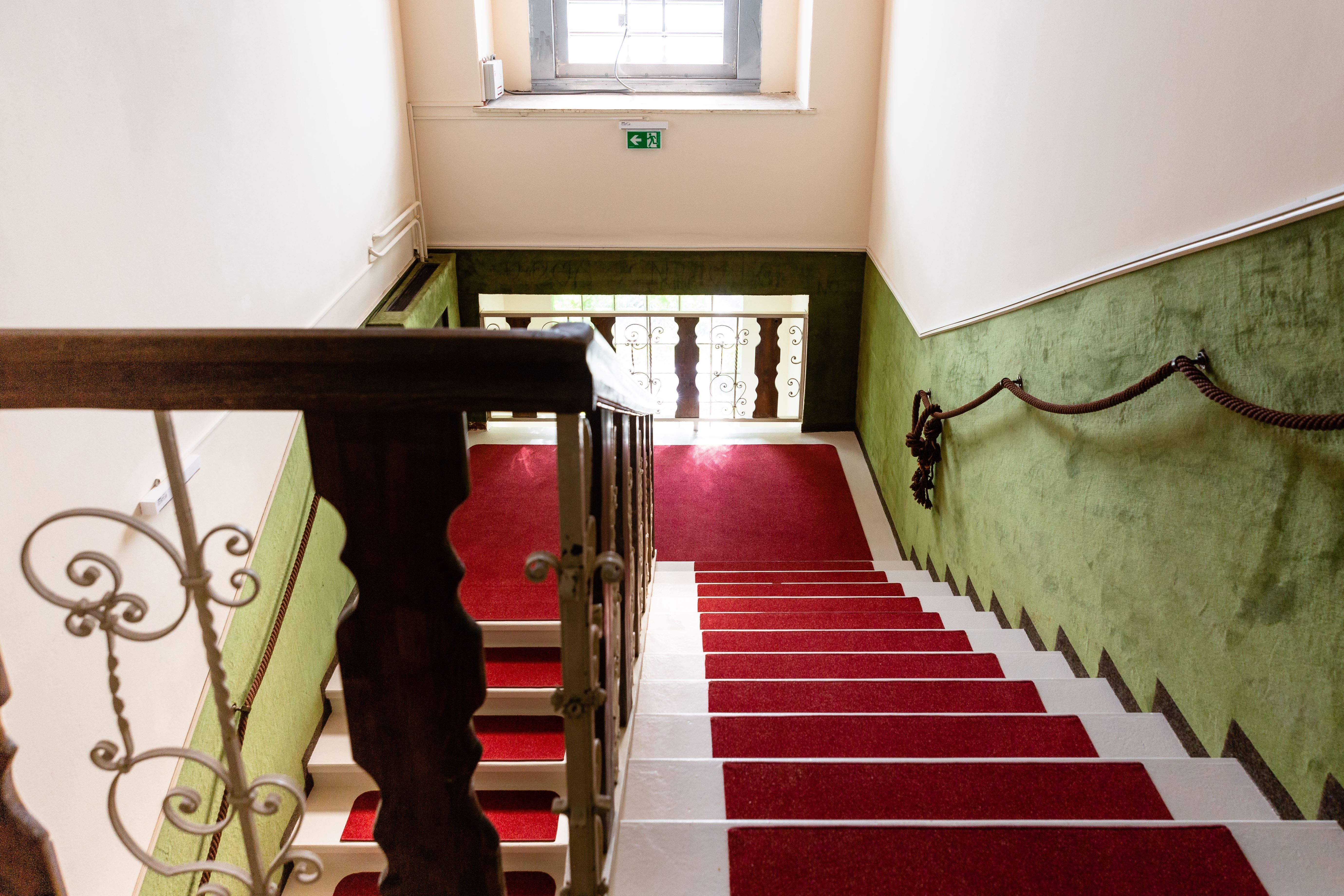 Treppenhaus mit rotem Teppich und grün gestrichenen Wänden.