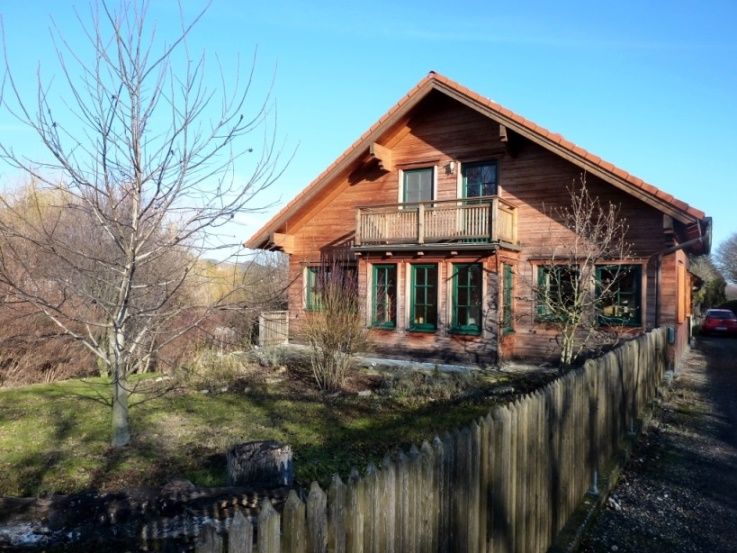 Holzhaus mit Balkon und Garten, umgeben von einem Holzzaun.