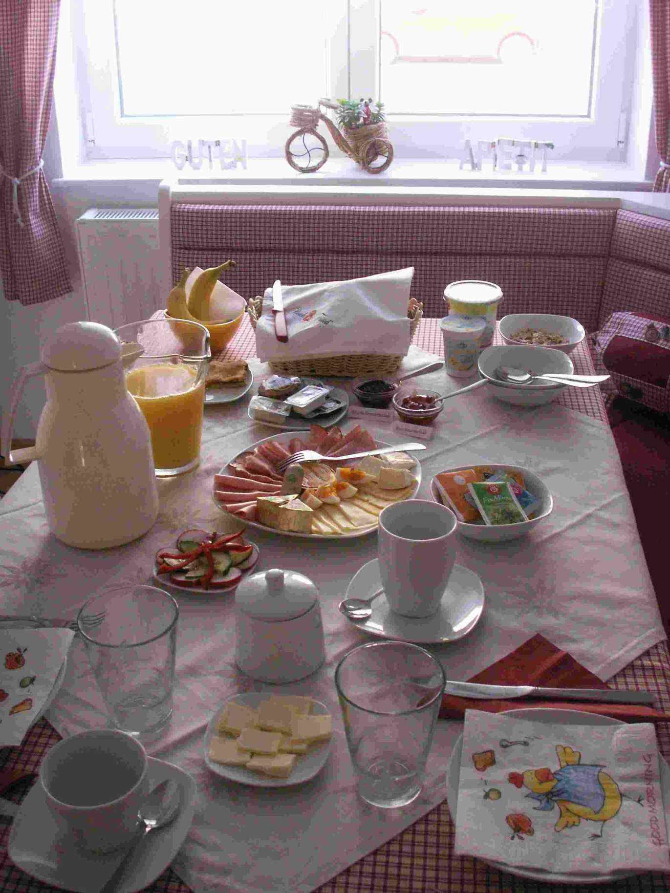 Ein gedeckter Frühstückstisch mit Brötchen, Aufschnitt, Käse, Saft und Geschirr.