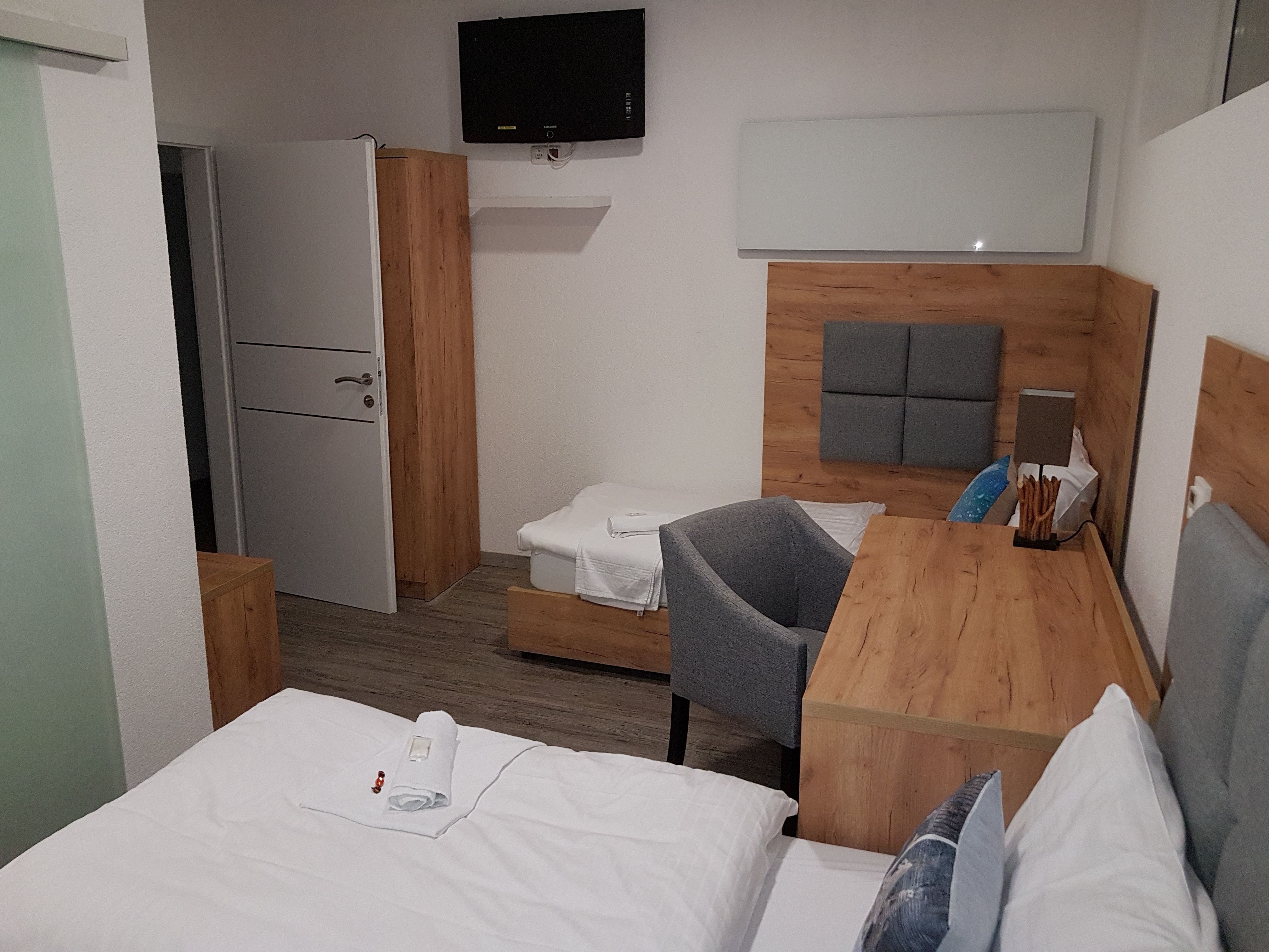 Hotelzimmer mit Holzmöbeln, zwei Betten, einem Schreibtisch und einem Fernseher an der Wand.