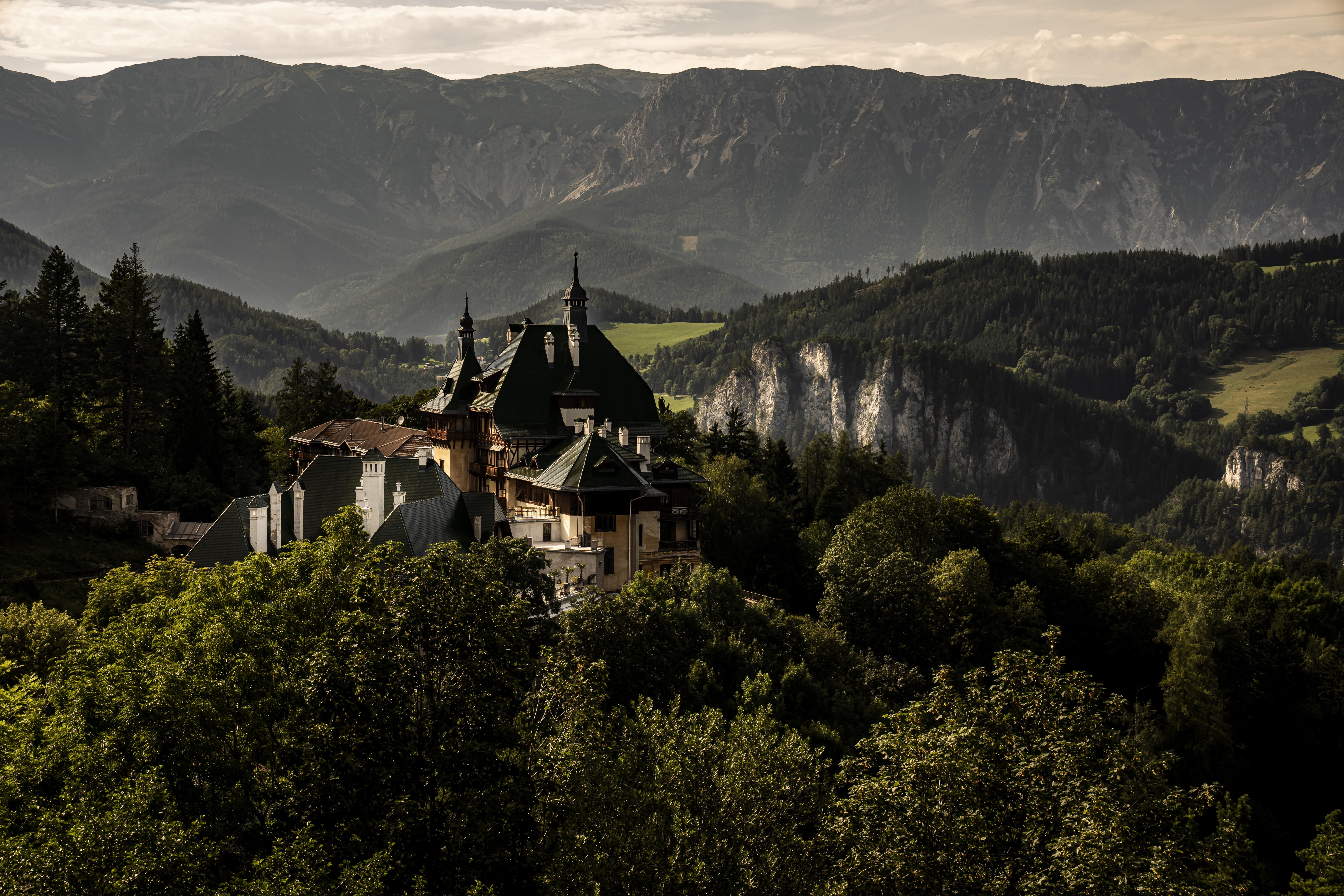 Historisches Hotel in den Bergen, umgeben von Wald und Bergen im Hintergrund.