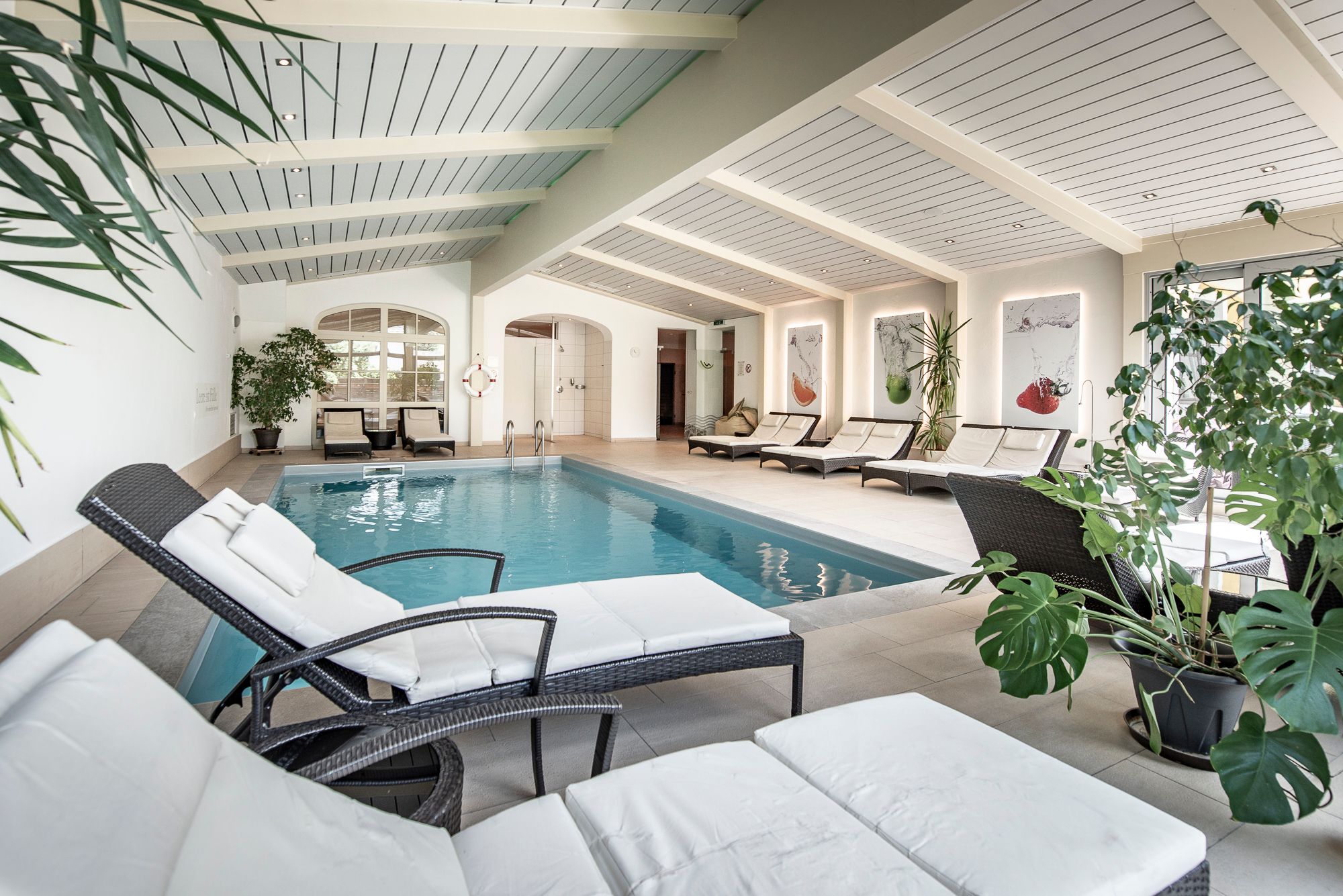 Innenansicht eines Hotelpools mit Liegestühlen und Pflanzen.