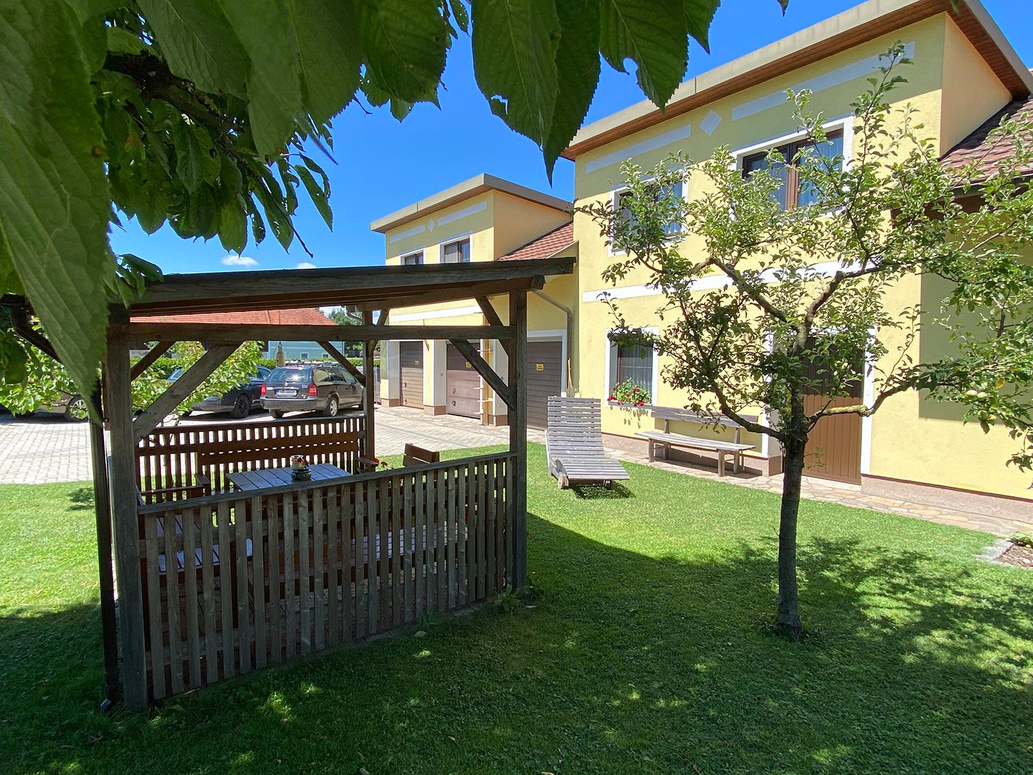 Garten mit Pavillon, gelbem Haus und Auto im Hintergrund.