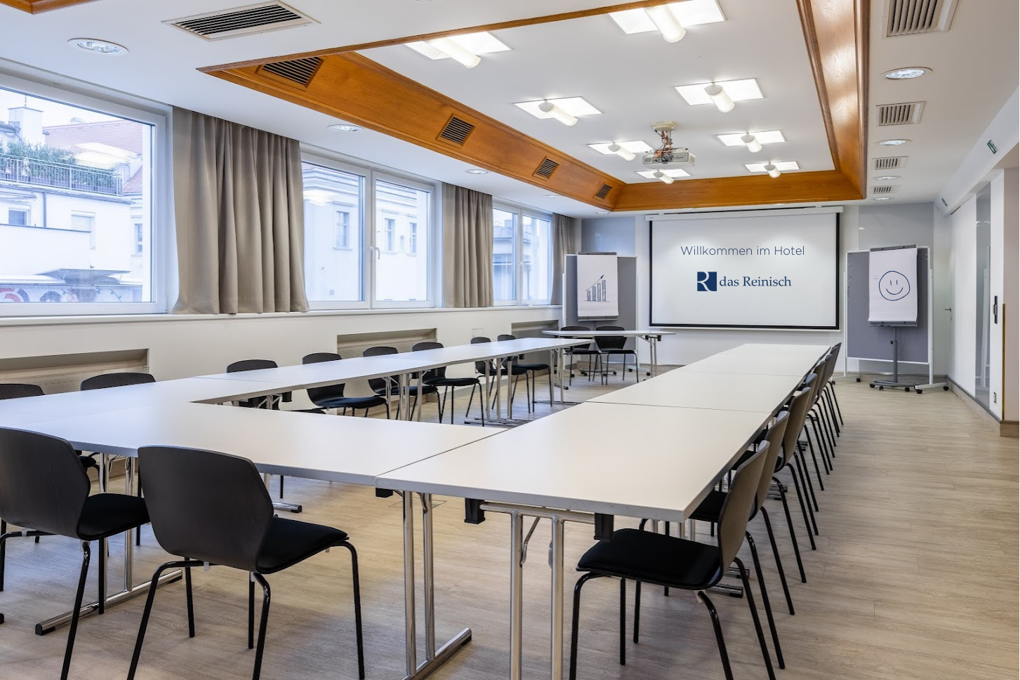 Seminarraum im Das Reinisch Hotel mit Tischen, Stühlen und Präsentationsleinwand.