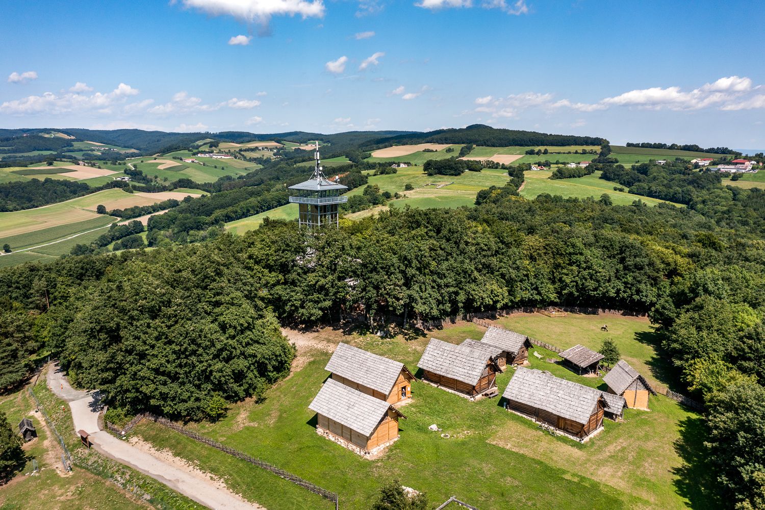 Luftaufnahme des Keltendorfs Schwarzenbach mit Aussichtsturm und nachgebauten keltischen Häusern, rundherum Wald und Wiesen.