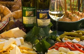 Heurigenjause mit Wein, Käse, Brot und Aufschnitt auf einem Tisch.