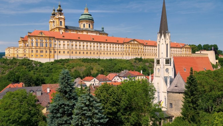 Blick auf das Stift Melk und die Pfarrkirche in Melk, umgeben von grüner Landschaft und blauen Himmel.