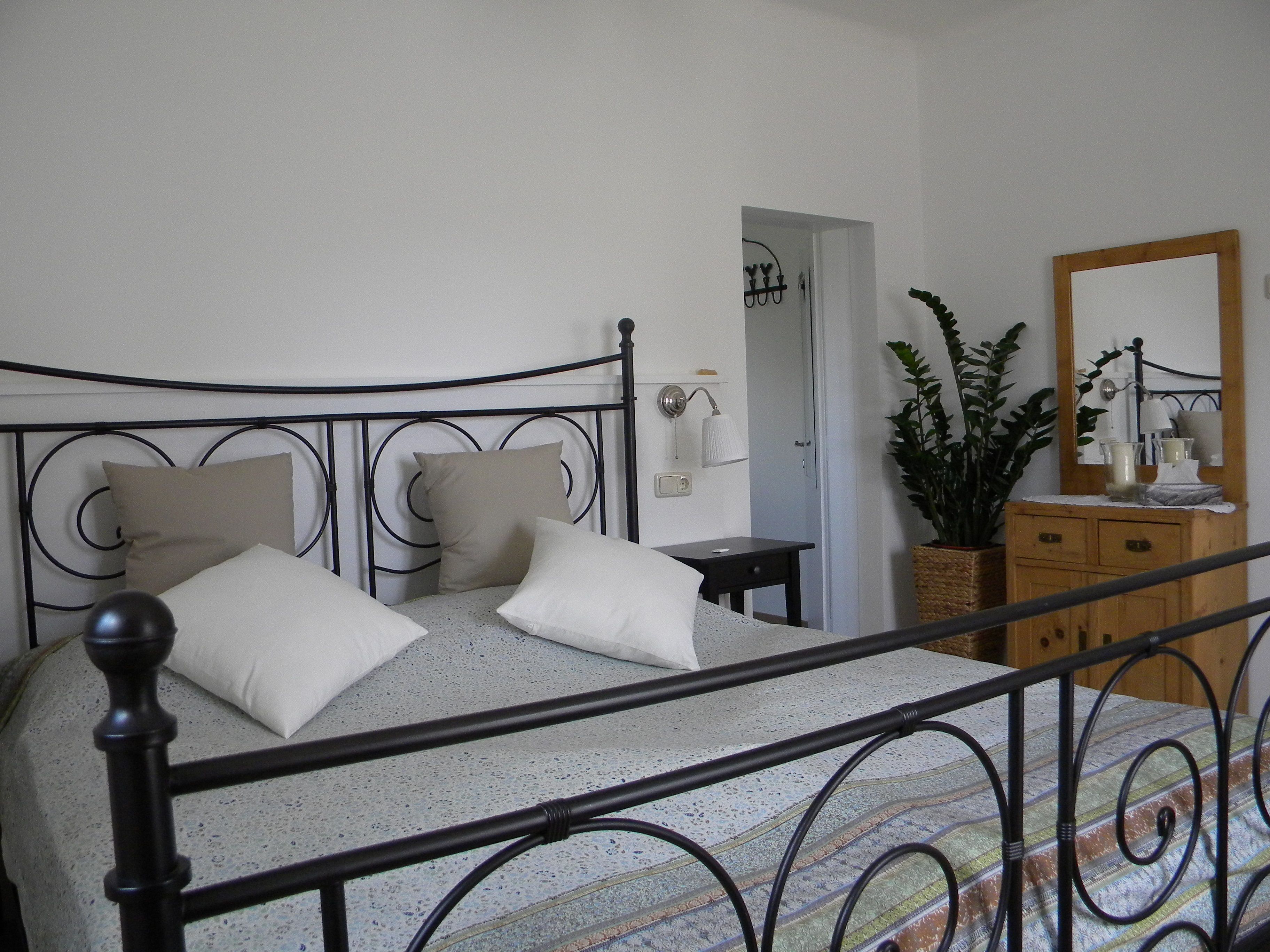 Schlafzimmer mit Metallbett, Kommode und Pflanze.