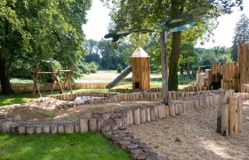 Spielplatz mit Holzspielgeräten und Rutsche im Freien.