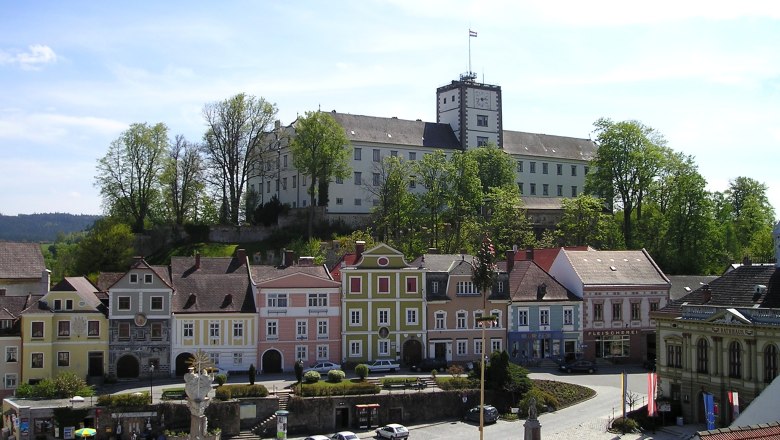 Blick auf den Hauptplatz von Weitra mit bunten Häusern und einem Schloss im Hintergrund.