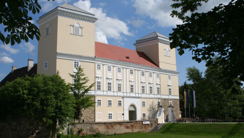 Schloss Wolkersdorf mit zwei T&uuml;rmen und rotem Dach, umgeben von B&auml;umen.