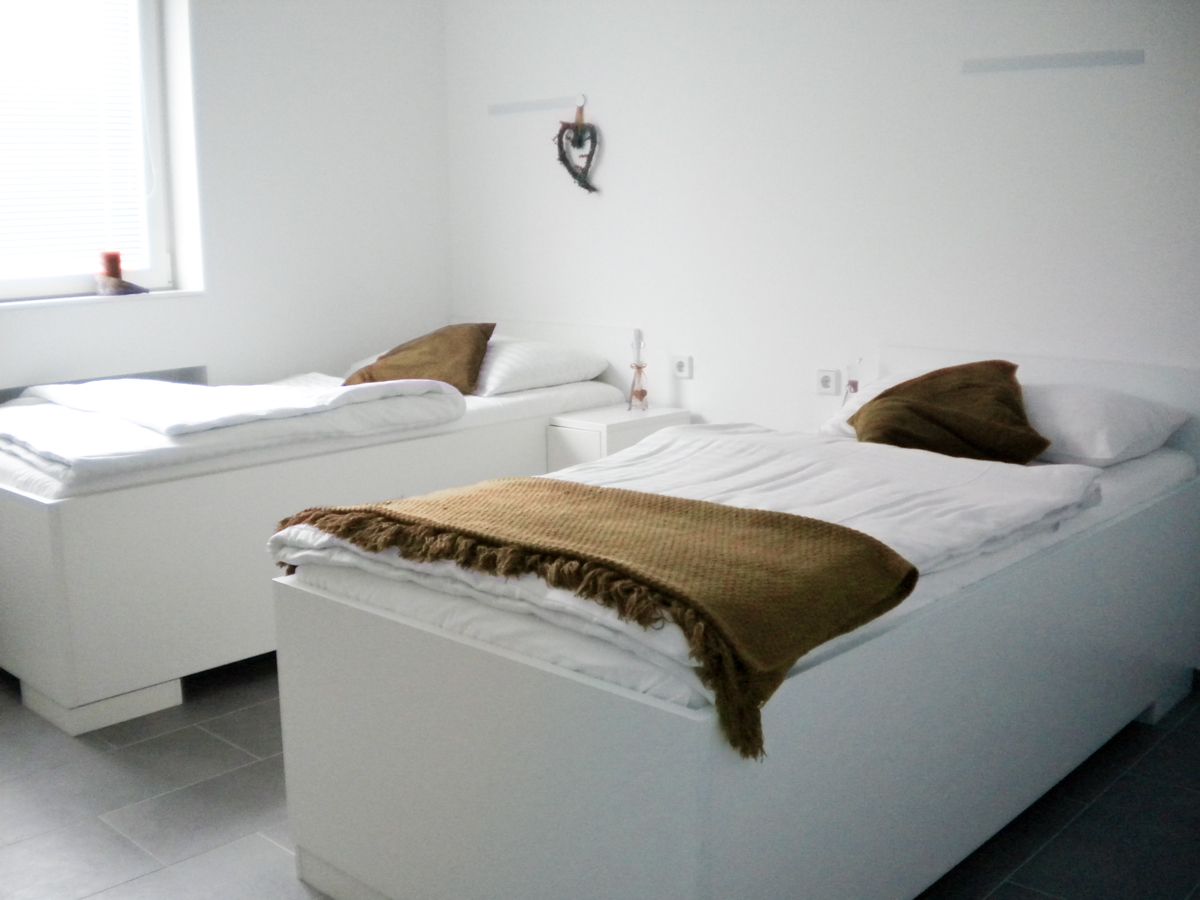 Zwei weiße Betten in einem hellen Raum mit braunen Decken und Kissen.