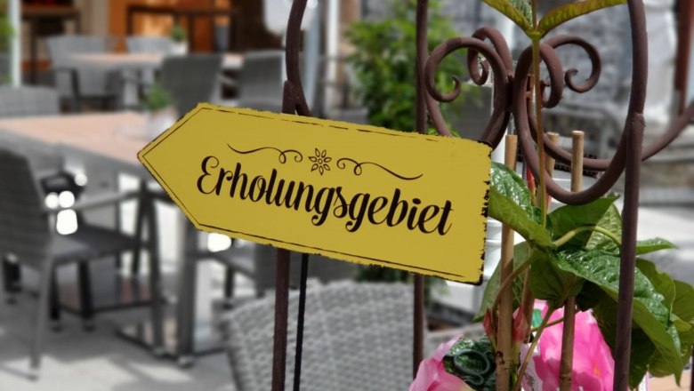 Ein Schild mit der Aufschrift 'Erholungsgebiet' in einem Caf&eacute;-Garten mit Tischen und St&uuml;hlen.