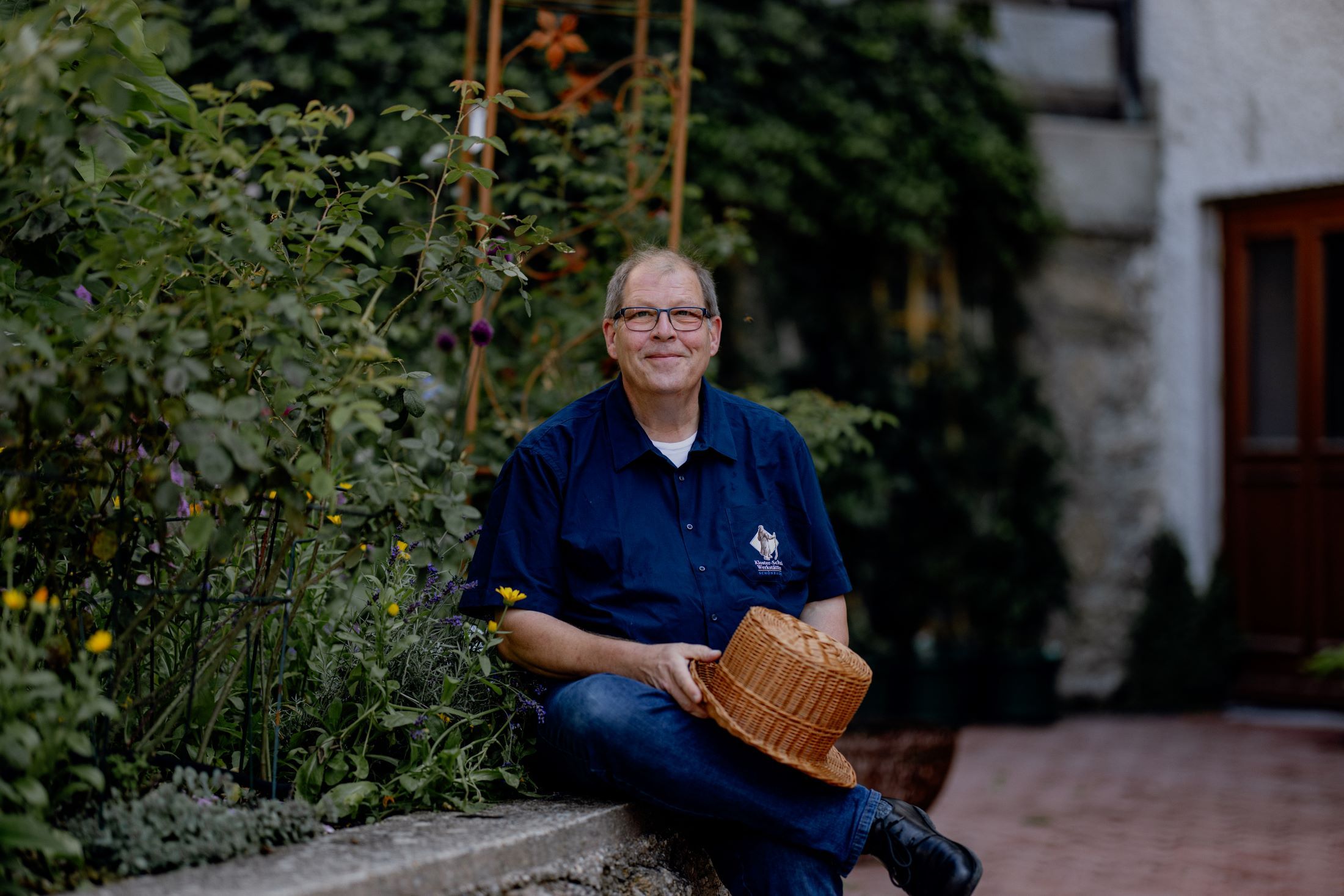 Ein Mann sitzt in einem Garten und hält einen geflochtenen Hut..