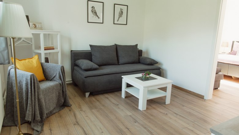 Modernes Wohnzimmer mit grauem Sofa, Sessel, weißem Couchtisch und Holzboden.