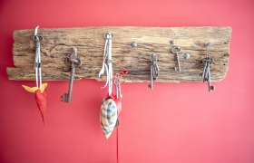 Alte Schlüssel hängen an einem rustikalen Holzbrett vor einer roten Wand.