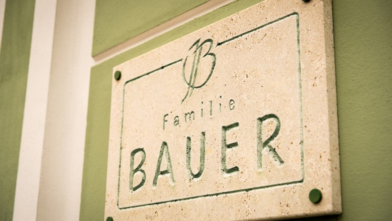 Steintafel mit der Aufschrift 'Familie Bauer' an einer gr&uuml;nen Wand.