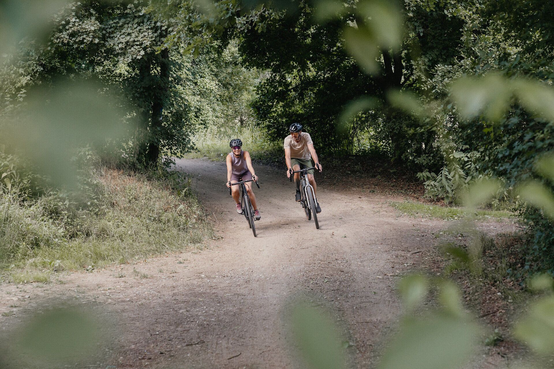 Zwei Radfahrer auf einem Waldweg in einer grünen Umgebung.