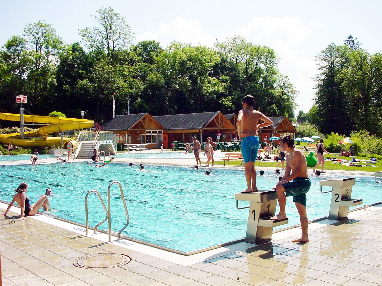 Freibad mit Schwimmern und Rutsche im Hintergrund.
