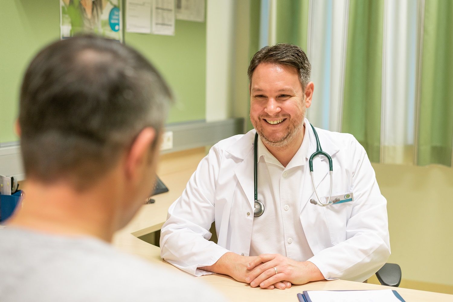 Ein Arzt im weißen Kittel lächelt einem Patienten zu, während sie an einem Tisch sitzen.
