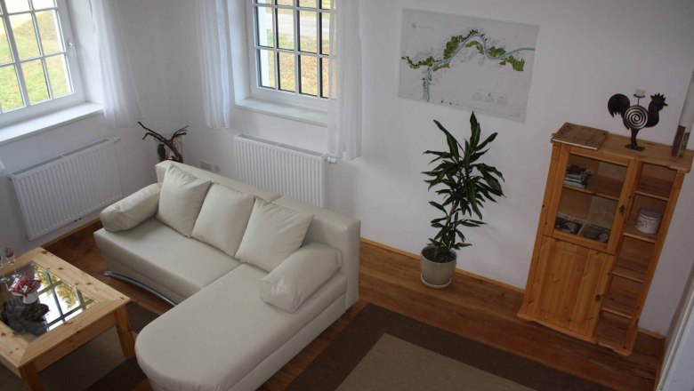 Gem&uuml;tliche Sitzecke mit beigem Sofa, Holztisch, Pflanze und Regal in einer Ferienwohnung.