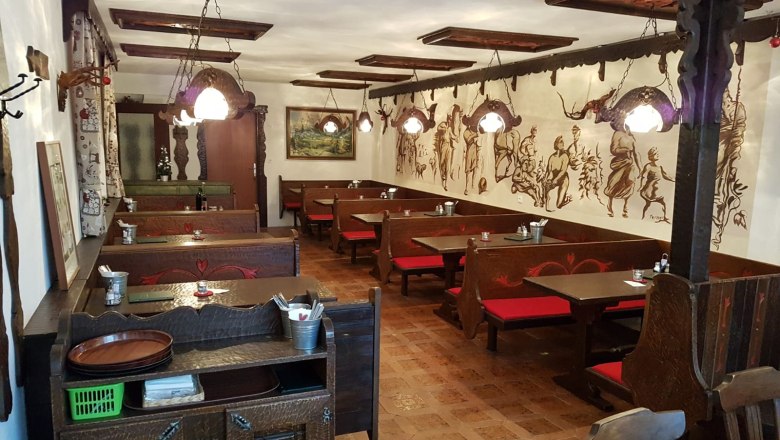 Innenansicht einer traditionellen Buschenschank mit Holzm&ouml;beln und Wandmalereien.