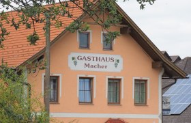 Ein traditionelles Gasthaus mit orangefarbener Fassade und roten Dachziegeln, umgeben von Bäumen.