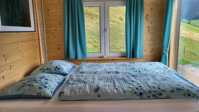 Holzinterieur mit Bett, Fenster und blauen Vorh&auml;ngen.