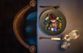 Ein Teller mit Schweinsmedaillons, lila Kartoffeln und Gemüse auf einem gedeckten Tisch.