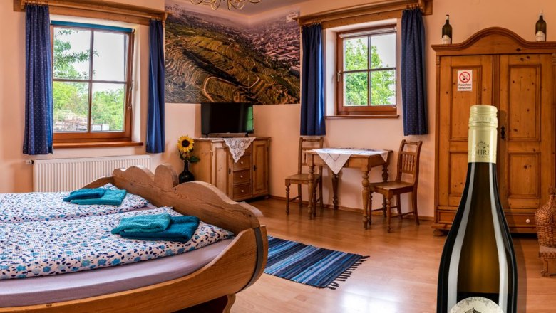 Gemütliches Zimmer mit Holzmöbeln, einem Fassbett und einer Weinflasche im Vordergrund.