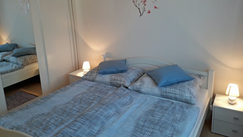 Gem&uuml;tliches Schlafzimmer mit Doppelbett, blauer Bettw&auml;sche, Nachttischen mit Lampen und einem Wandtattoo mit Blumen und V&ouml;geln.