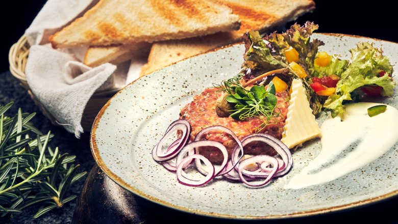 Ein Teller mit Beef Tatar, Zwiebelringen, Salat und Toastscheiben.