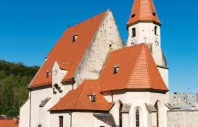 Wehrkirche Edlitz mit vielen Seitenbereichen, roten Ziegeld&auml;chern, einem spitzen Turm und blauem Himmel.