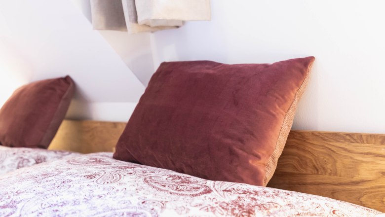 Nahaufnahme eines Bettes mit roten Kissen und gemusterter Bettw&auml;sche.