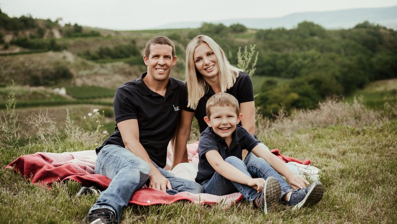 Familie sitzt auf einer Decke im Freien mit grüner Landschaft im Hintergrund.