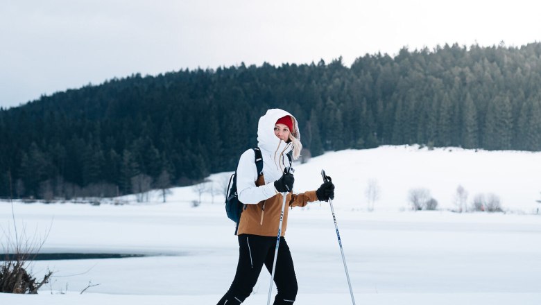 Eine Person beim Skilanglauf auf einem verschneiten Feld vor einem Wald.