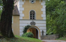Historisches Geb&auml;ude mit Turm und Uhr in einem Waldgebiet.