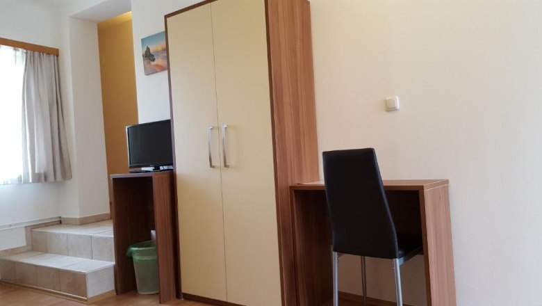 Ein einfacher Raum mit Schreibtisch, Stuhl, Kleiderschrank und kleinem Fernseher.