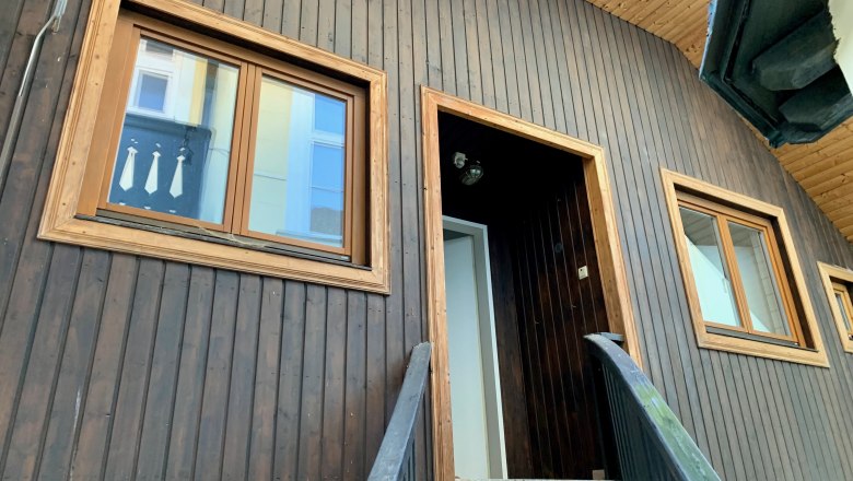 Nahaufnahme einer Hausfassade mit Holzwand und Fenstern.