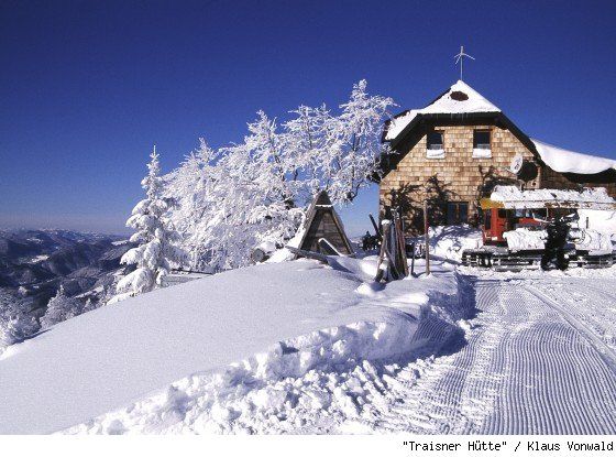 Verschneite Berghütte mit schneebedeckten Bäumen und klarem blauen Himmel.