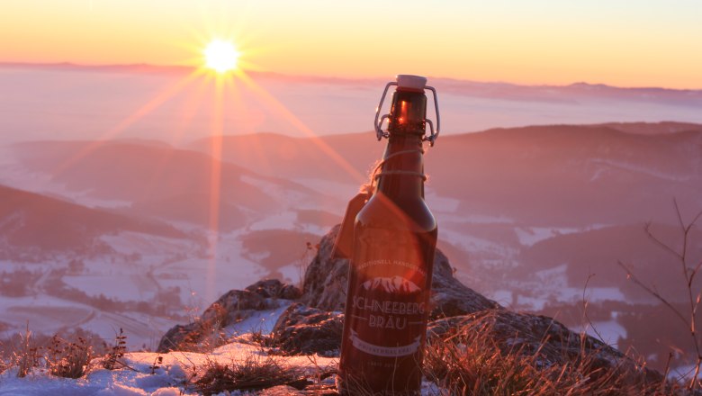 Eine Flasche Schneeberg Br&auml;u Bier steht auf einem schneebedeckten Berg bei Sonnenuntergang.