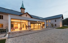 Modernes Gebäude mit Glasfassade und historischem Turm im Hintergrund.