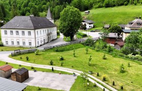 Landschaft mit historischem Gebäude, grünen Wiesen und Bäumen.