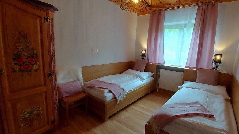 Gem&uuml;tliches Schlafzimmer mit zwei Einzelbetten, Holzm&ouml;beln und rosa Vorh&auml;ngen.
