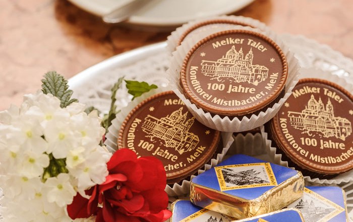 Ein Teller mit Pralinen und einer Tasse Kaffee im Hintergrund.
