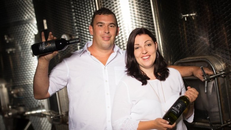 Ein Winzerpaar im Weinkeller mit Weinflaschen in der Hand.