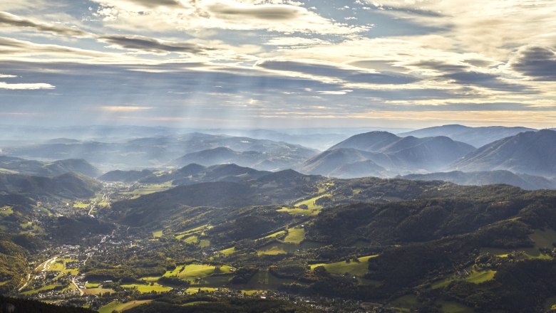 Panoramablick auf die Raxalpen mit Sonnenstrahlen und Wolken am Himmel.