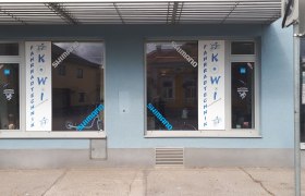 Fahrradgesch&auml;ft mit blauer Fassade und Schaufenstern mit Aufschrift 'Fahrradtechnik KOWI'.