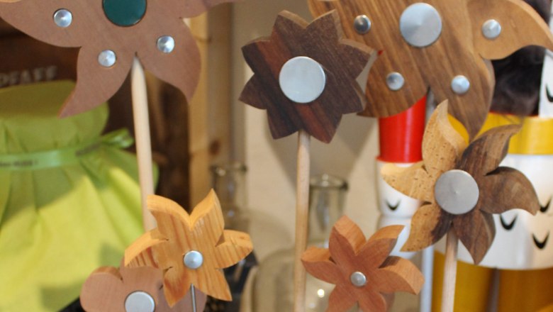 Holzblumen mit Metallverzierungen auf St&auml;ben in einem Regal.